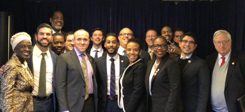 Brooklyn's 16-member City Council delegation, dressed in suits, poses for a light-hearted group photo. 