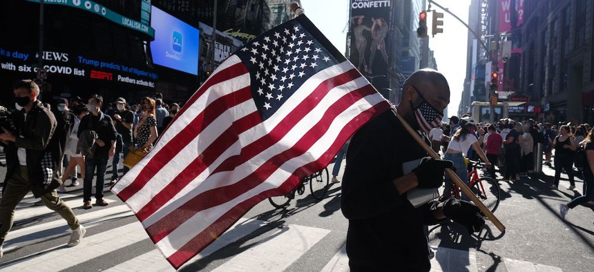 A man carries an American flag as people gather in Times Square in New York City to celebrate the election of Joe Biden as the 46th President of The United States.
