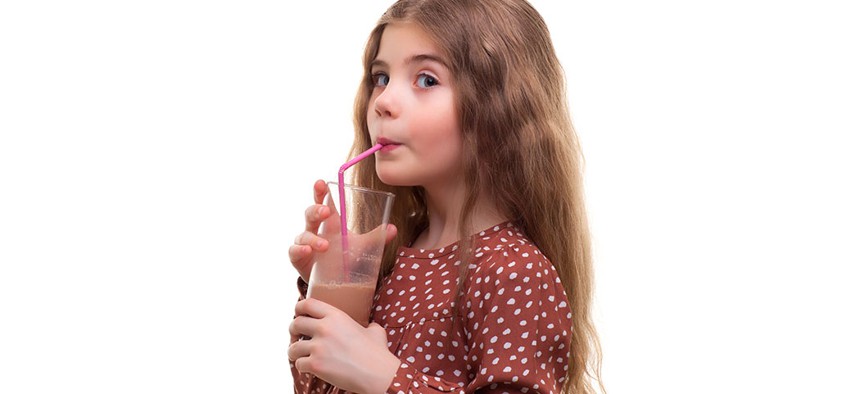 A young girl drinking chocolate milk.