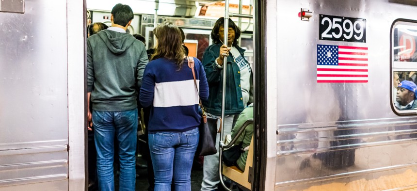 A New York City subway car with people standing close together in front of open door. 