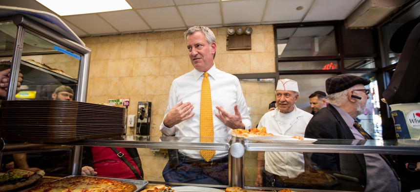 Mayor de Blasio contemplating whether to eat his slice with a fork or not.
