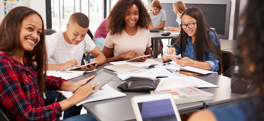 Teacher sitting with high school students using tablets.