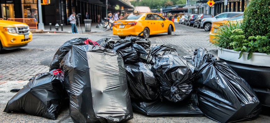 Black bags of trash on sidewalk in New York City street waiting for service trash truck. 