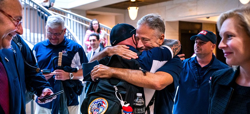 Jon Stewart hugs 9/11 first responder John Feal while U.S. Sens. Chuck Schumer and Kirsten Gillibrand look on, after the Senate's passage of the 9/11 Compensation Fund. 