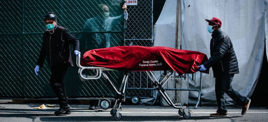 Hospital employees and funeral service employees transfer a body from a temporary mobile morgue, put in place due to lack of space at the hospital, into a funeral home vehicle outside of the Brooklyn Hospital Center in Brooklyn.