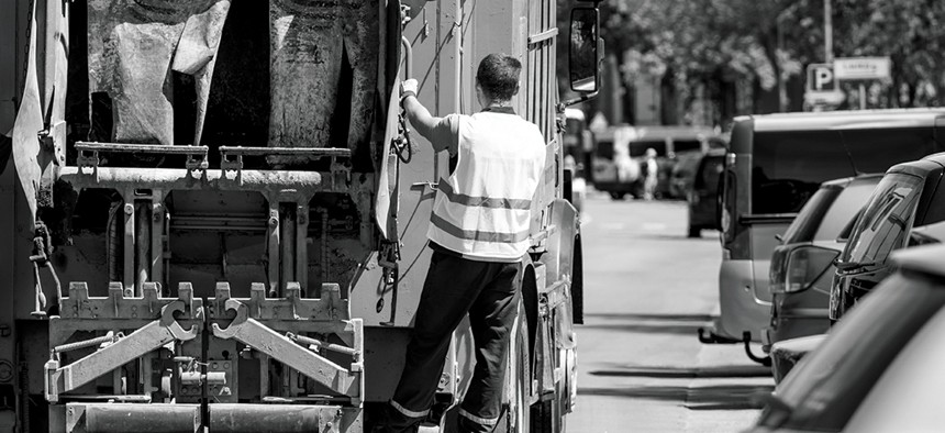 A man riding on the back of a garbage truck