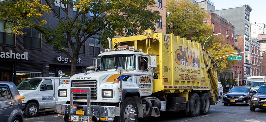 A big yellow private sanitation truck driving through the streets of Manhattan.