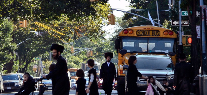 Orthodox Jewish children and adults cross a street in front of a school bus in Borough Park, Brooklyn.