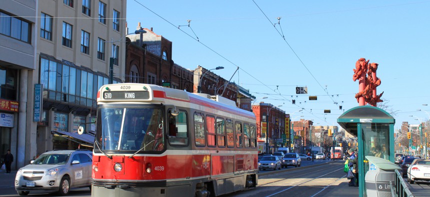 A red streetcar in Toronto's Chinatown with overheard wires and a station in the middle of the road. 
