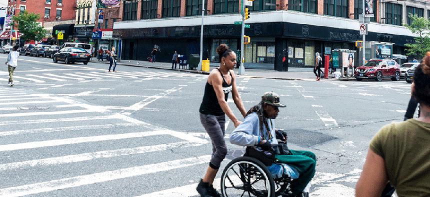 A young woman pushes a man in a wheelchair across the street.