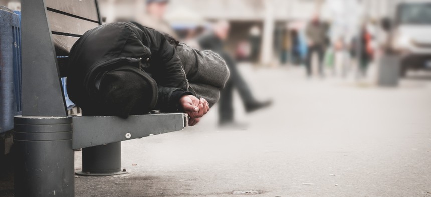 A homeless person sleeps on a bench.