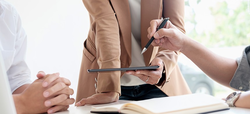 Employees point at notebooks around conference table.