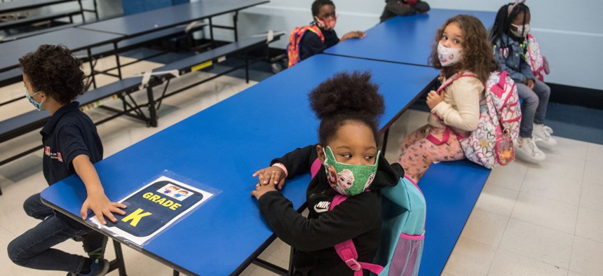 New York City elementary school students sitting at cafeteria table with masks on.