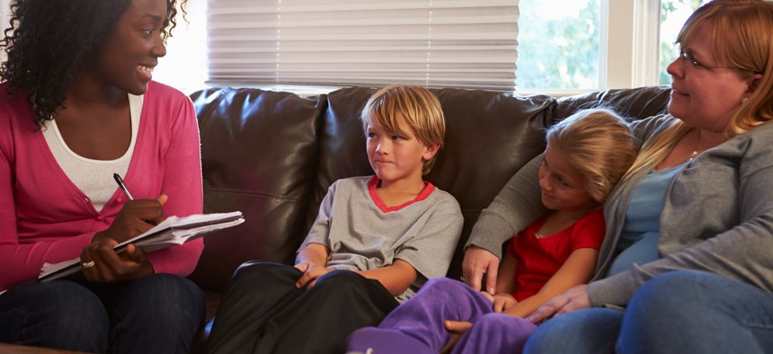 Social worker wearing pink shirt smiles at family of three, one daughter, one son and their mother