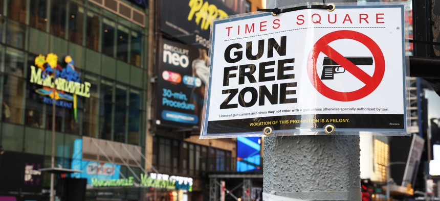People walk past a "Gun Free Zone" sign posted on 40th Street and 7th Avenue in New York City