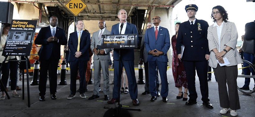 MTA chair Janno Lieber (center) announced a new public service campaign to discourage subway surfing at a press conference in Queens. Google and YouTube will provide the city with free ad space to publicize the campaign, which was designed by Milana Blokhina (right), a student at the High School of Art and Design.