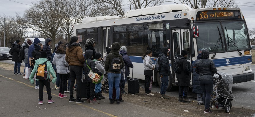 Migrants wait at a bus stop outside of Floyd Bennet Field.