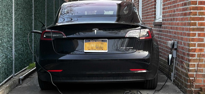 A Tesla parked in driveway and plugged into charger in Queens, New York.