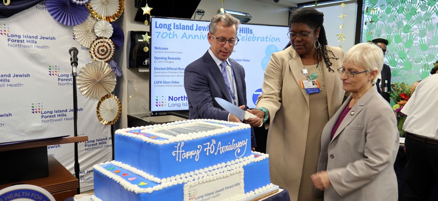 John D’Angelo, senior vice president and regional executive director at Northwell, helps Lorraine Chambers Lewis, executive director of Northwell Long Island Jewish Forest Hills in Queens and Council Member Lynn Schulman celebrate the hospital’s 70th anniversary of serving the health care needs of the community in August 2023. 